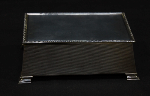 A silver cigarette box of rectangular form, with sloped sides, raised on bracket feet, with cast