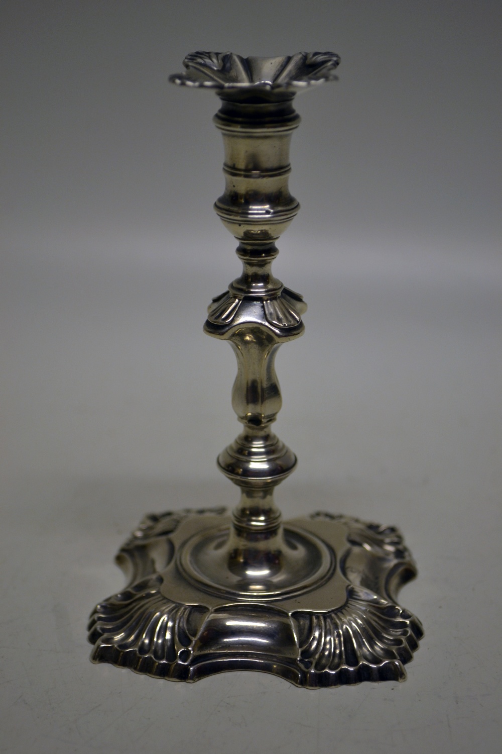 A George II cast silver taperstick four shell decorated panelled knopped stem, the spool shaped