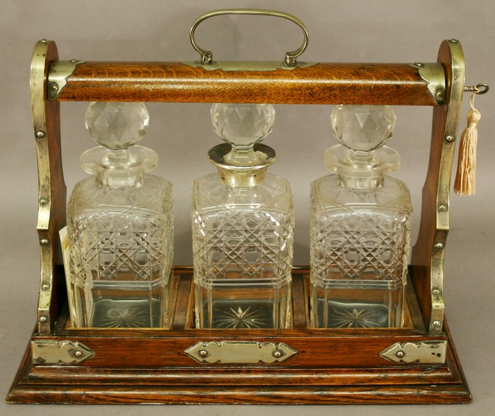 AN EDWARDIAN OAK THREE-BOTTLE TANTALUS of typical form with locking mechanism, three square