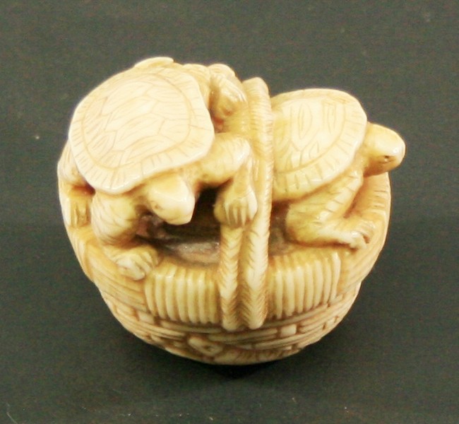 A JAPANESE CARVED IVORY NETSUKE carved as a basket of turtles, bearing signature to base.  3.5cm