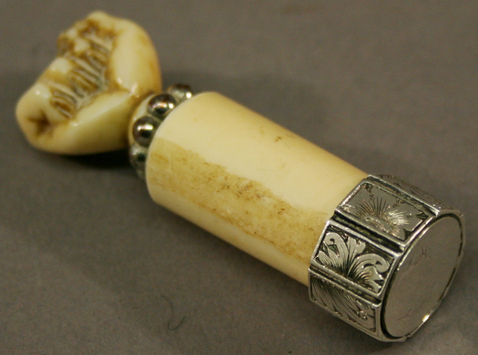 A 19TH CENTURY WHITE METAL MOUNTED IVORY SEAL having a terminal carved as a clenched fist, a beaded