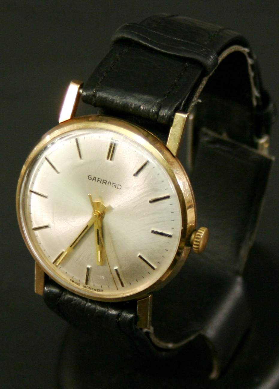 A 9CT GOLD CASED GARRARDS WRISTWATCH of circular form, the silvered dial with baton markers and