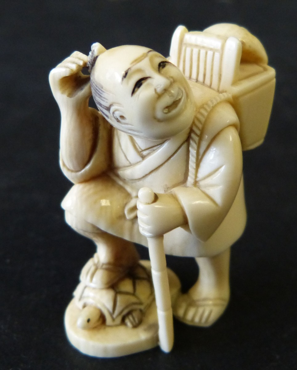 An Ivory Netsuke in form of a standing gentleman carrying a basket upon his back with mask, 5cm