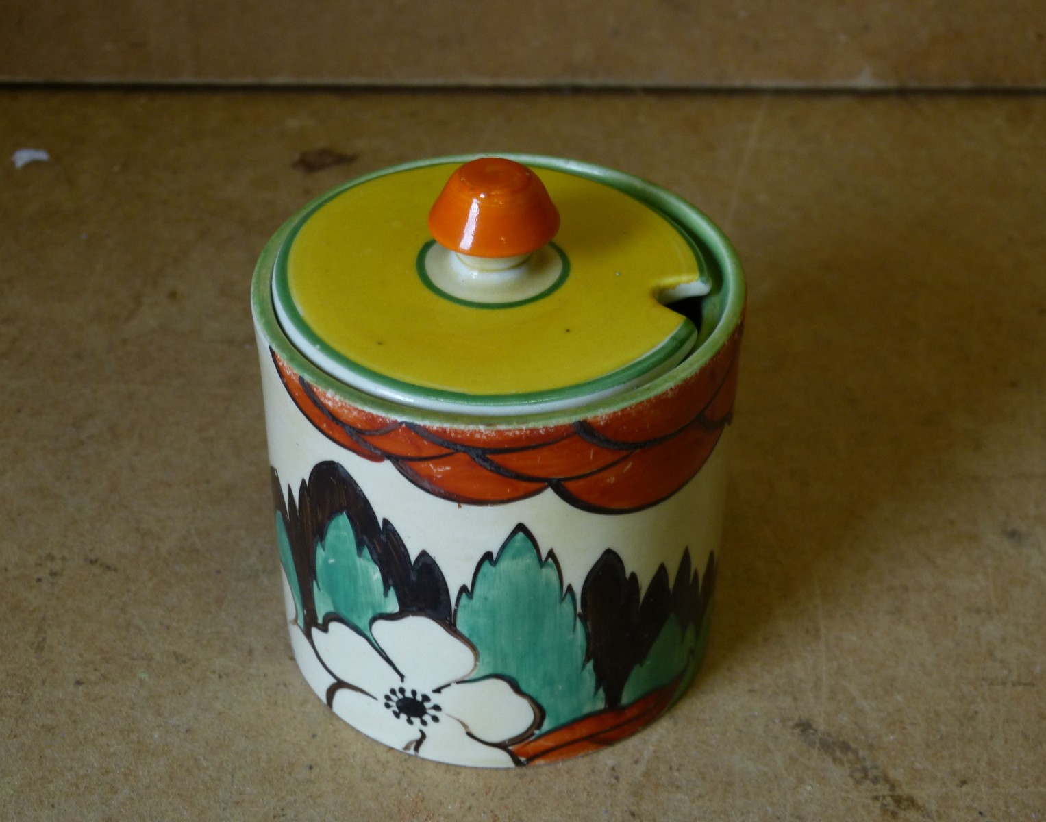 A Clarice Cliff Round Lidded Jam Pot, having multicoloured tree, floral and leaf decoration, 9cm