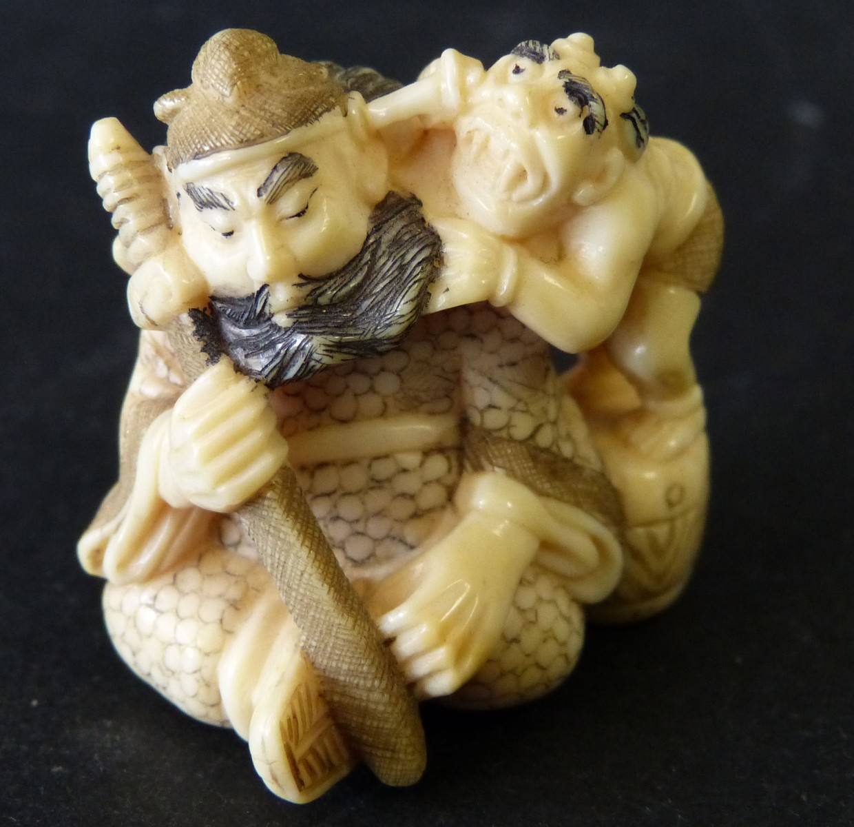 An Oriental Netsuke in form of a seated warrior, with demon standing next to him, 3.5cm high