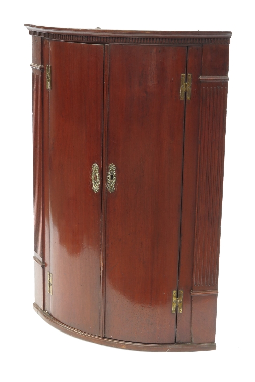 A Georgian mahogany bow front corner cupboard, with reeded sides, opening to reveal three shelves,