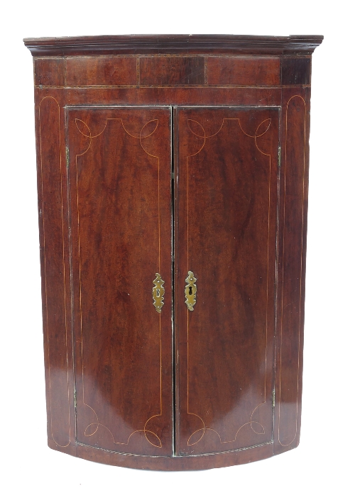 A Georgian mahogany bow front corner cupboard, having two doors with boxwood line inlay, opening