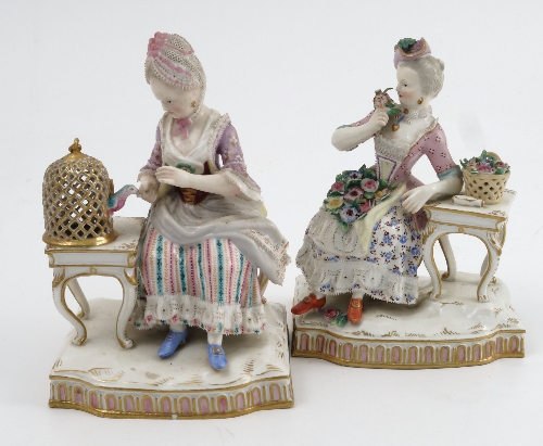 A pair of 19th century Meissen porcelain figures, depicting ladies sitting by tables, one with a