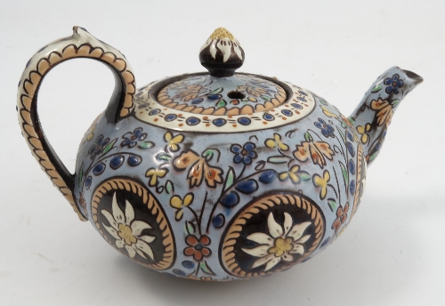 A pottery tea pot, decorated with flowers to a pale blue ground, the base marked J Pioune, height