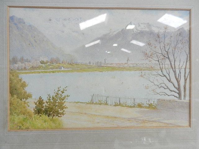 An early 20th century watercolour depicting a lake with village and mountains to background