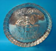 A circular silver dish embossed with scene depicting cherubs and a goat with crimped edge, 19cm