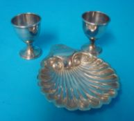 A pair of silver egg cups and a silver scallop shell butter dish, 150g