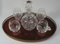 A cutglass branded decanter with 4 glasses on a wooden brass tray