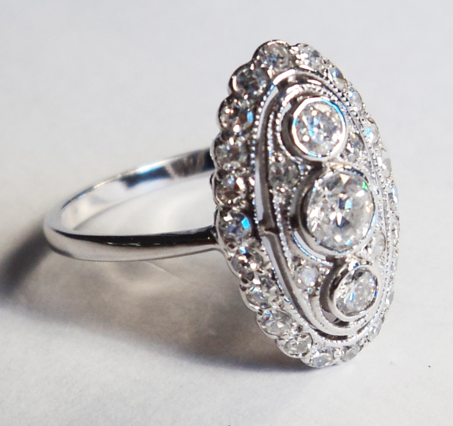 An 18ct. white gold oval panel ring, set with three central diamonds within a diamond boarder