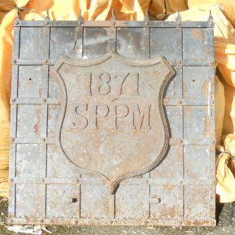 A cast and wrought iron portcullis pattern fire back with applied boundary marker with shield