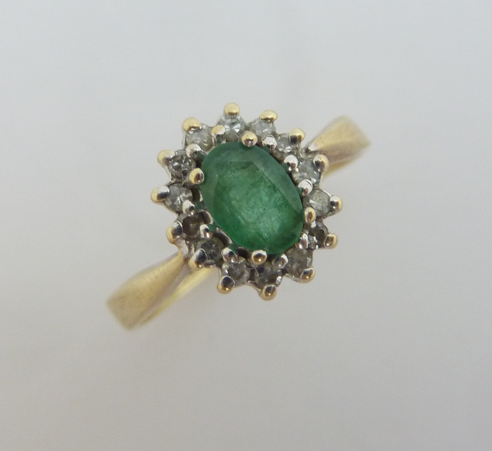 A 9CT GOLD EMERALD AND DIAMOND RING, an oval shape emerald with a surround of single cut diamonds,