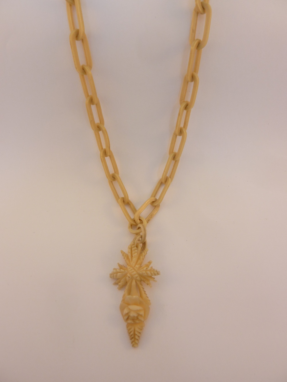 AN IVORY NECKLACE, with oval shape links to the carved crucifix stylised as wheat and roses, length