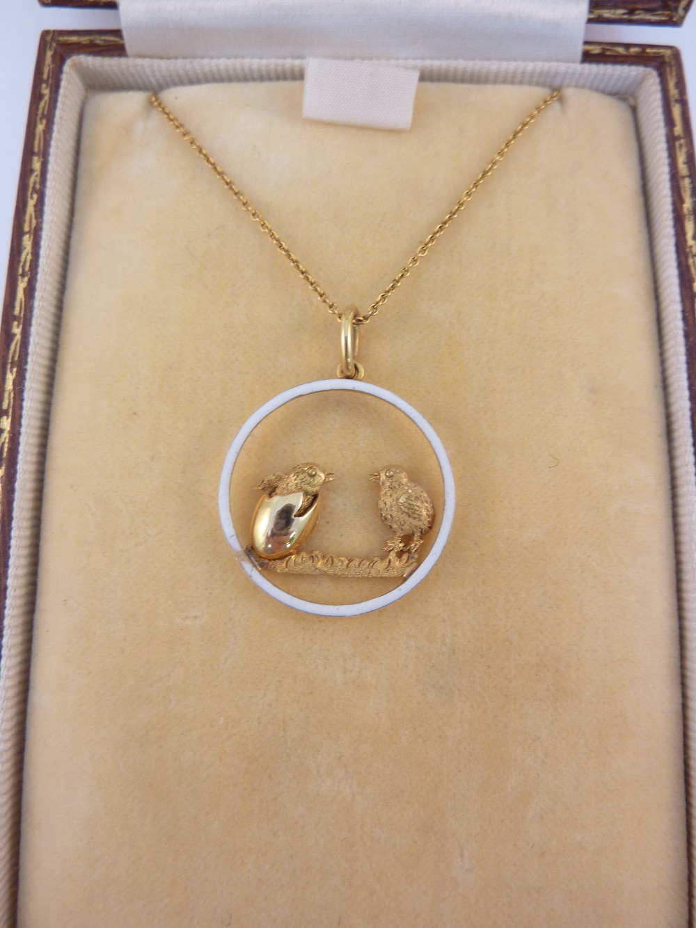 A LADIES PENDANT, depicting a bird watching a chick hatch within a white enamel circle, suspended