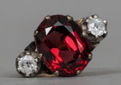 An unmarked gold, diamond and ruby three stone ringThe central facet cut red stone flanked by two