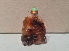 A Chinese carved agate snuff bottle
Worked with a mythical beast, the cover green stone inset.  6