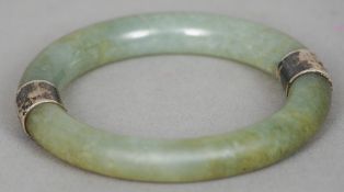 A Chinese unmarked silver mounted jade bangle
Set to either side with a small silver slip.  7.5
