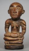 A small carved hardwood tribal figure
Formed as a seated woman with glass inset eyes, holding a