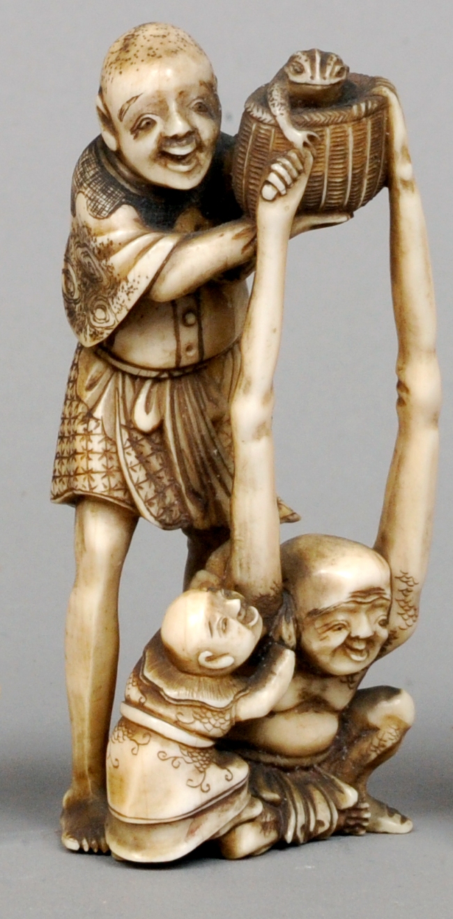 A Japanese ivory okimono
Carved as Tenaga and Ashinaga holding aloft a toad in a basket from the