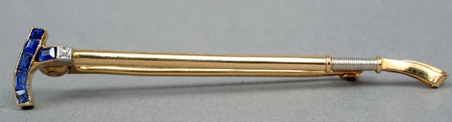 An unmarked gold, diamond and sapphire set bar brooch
Formed as a riding crop.  5.25 cms wide.