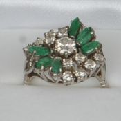 An 18 ct white gold diamond and emerald cluster ring The central diamond spreading to