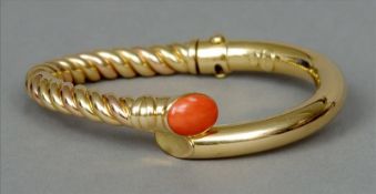 An 18 ct gold designer torque bangle The half spiralled band set with a coral cabochon. 8 cms