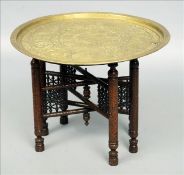 A late 19th century Eastern brass topped folding table The circular top decorated in relief with
