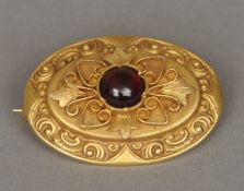 A Victorian unmarked yellow metal garnet set brooch The central cabochon stone above the scrolling