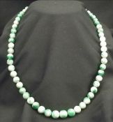 A green jadeite necklace With sixty-one round beads, the clasp set with three brilliant cut