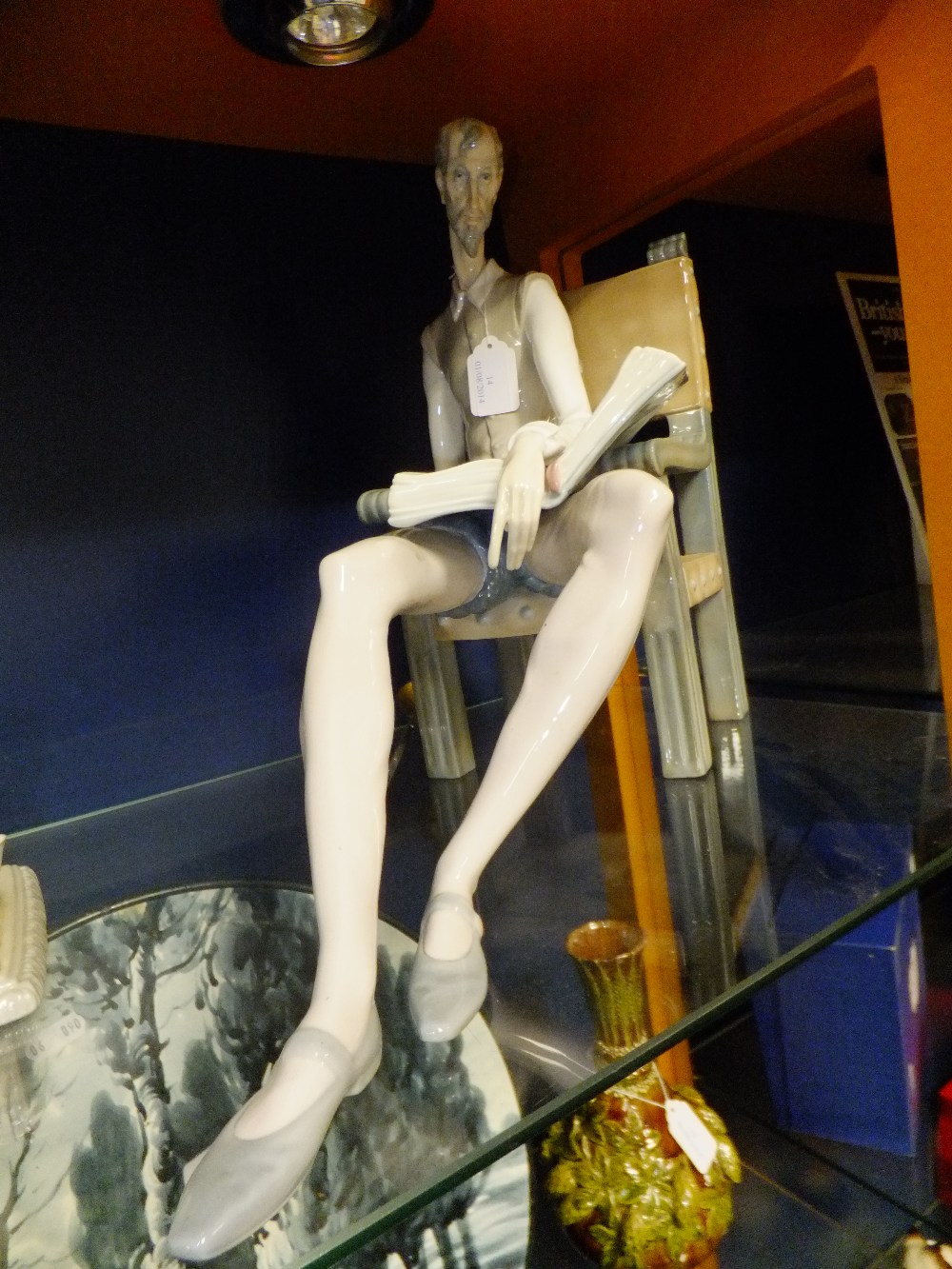 A Lladro figure of "Don Quixote" sitting in a chair reading his book whilst holding his sword in his