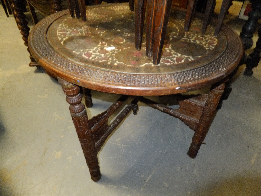 An ornately carved Indian hardwood folding occasional table with inset brass top