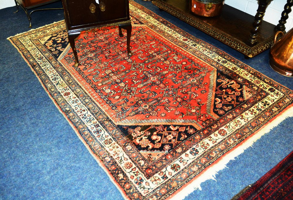A Persian rug with geometric design over red ground, spandrels and triple floral border, 214 x