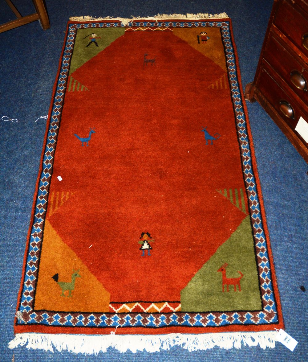 An Indian rug, the red ground with simple spandrels decorated with people and animals, borders,