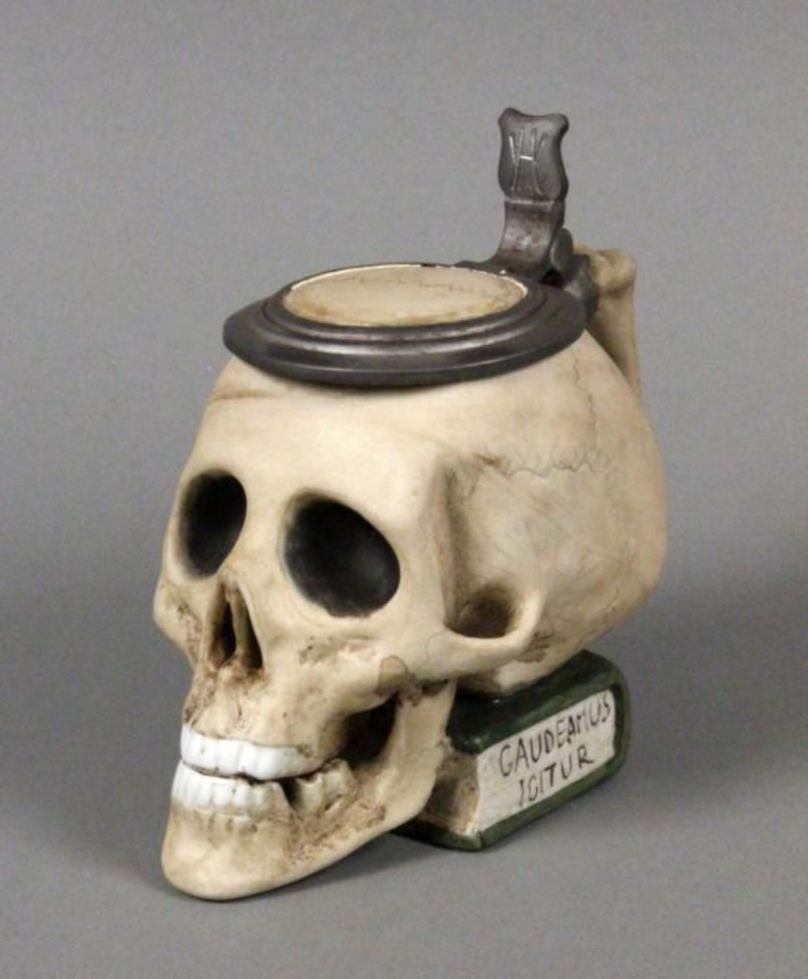 A STUDENT TANKARD IN THE FORM OF A SKULL made of porcelain with mounted pewter cover, painted,