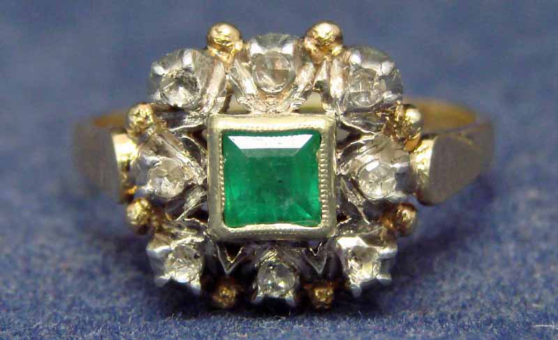 An 18ct gold cluster ring centrally set with a square cut emerald within a yellow gold collar