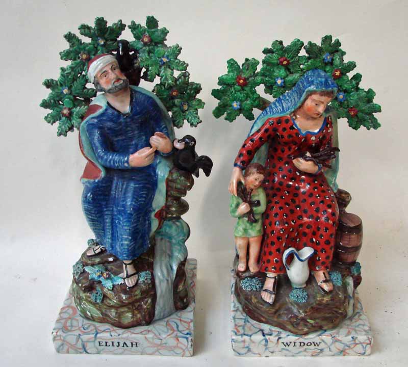 A pair of 19th century Staffordshire pottery figures, Elijah and Widow, both seated in naturalistic