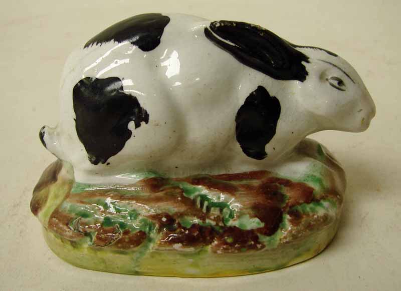 A Victorian Staffordshire pottery model of a black and white crouching rabbit, ears laid back, on