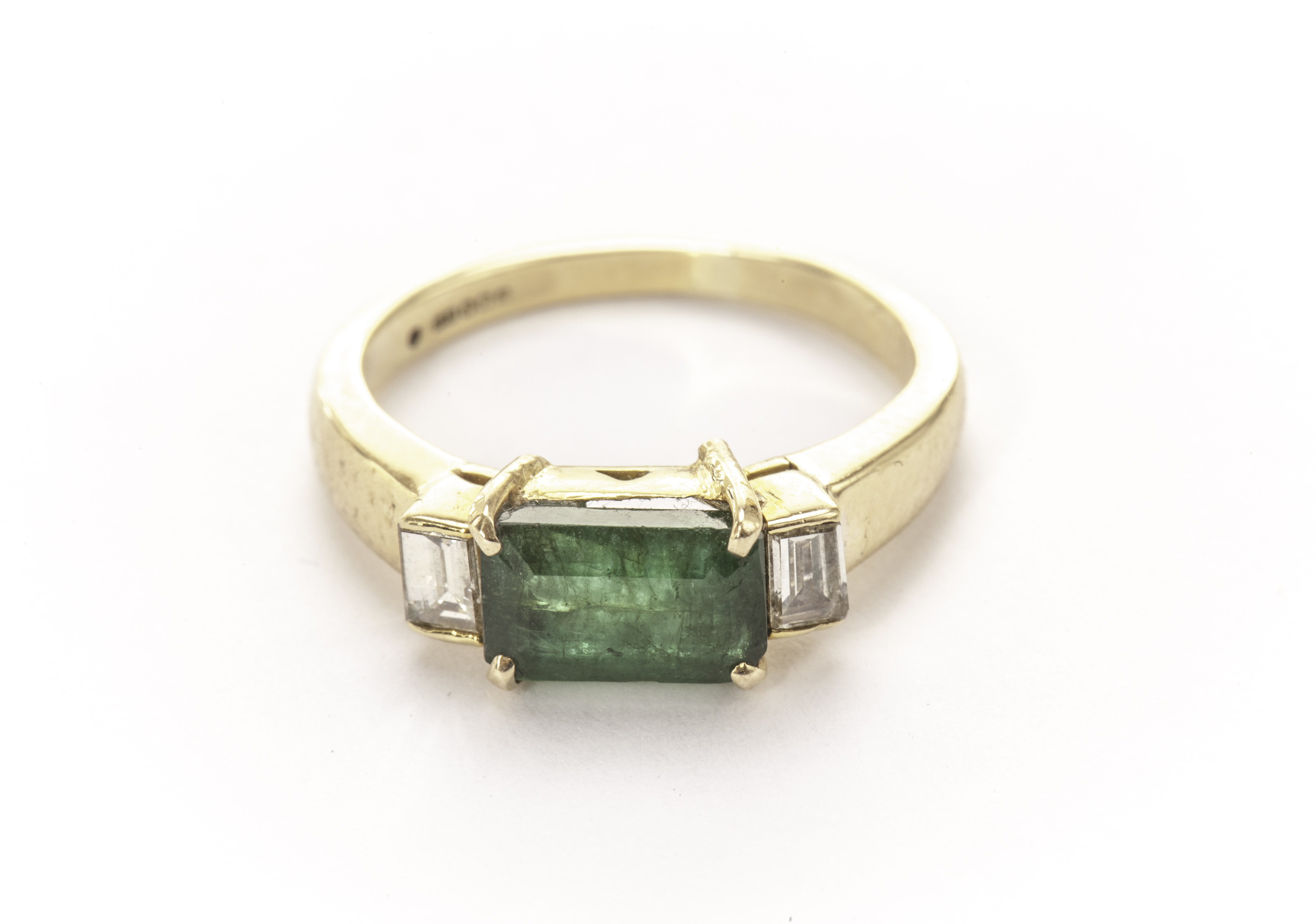 An Art Deco style emerald and diamond three stone ring, the rectangular green stone flanked by a