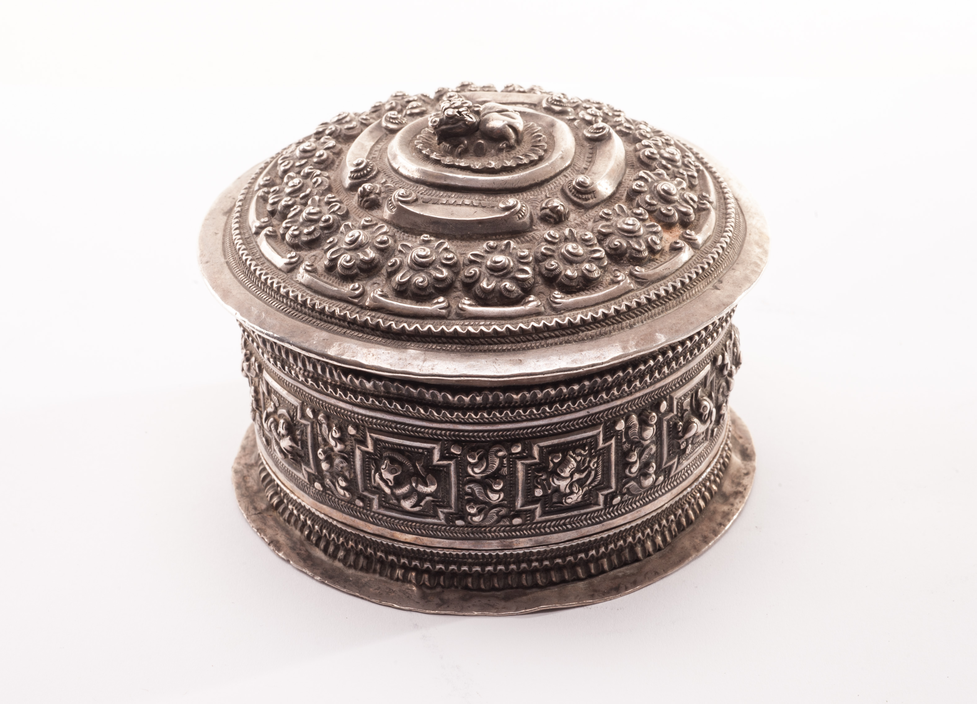 A circular silver Tibetan scroll box, the lid with embossed floral motif and dog of fo finial, the