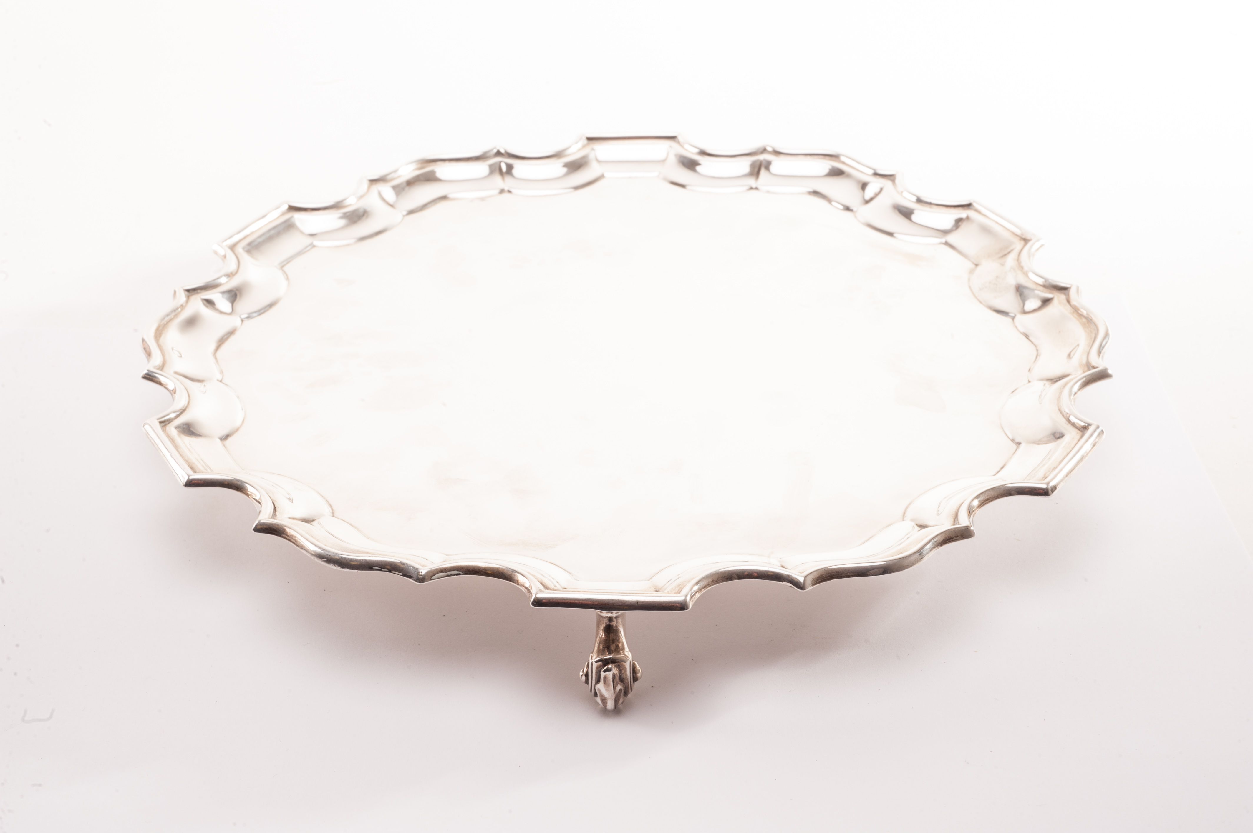 A George V silver salver from Jays of Oxford Street, scalloped rim with plain well, supported on