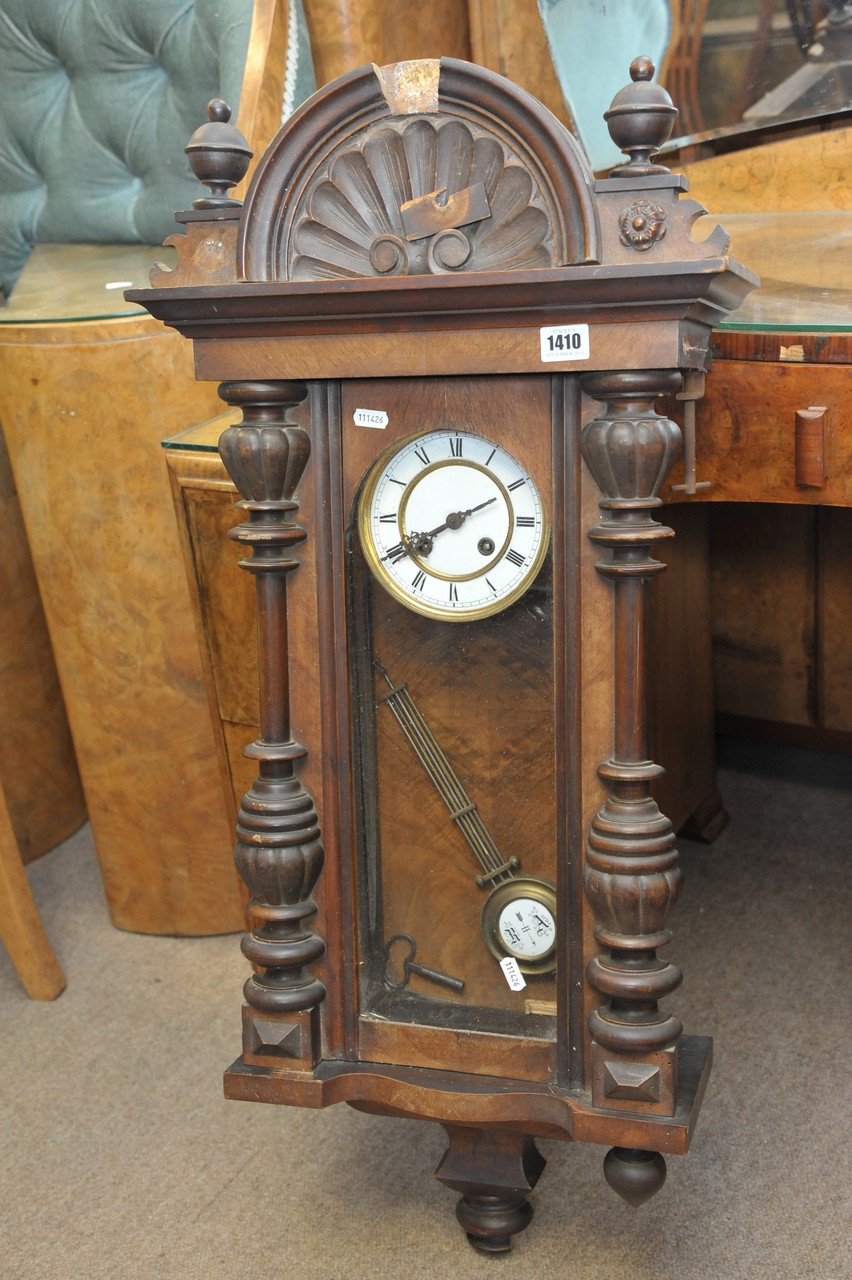 A continental walnut wall clock with a shaped pediment and enamel dial with visible pendulum