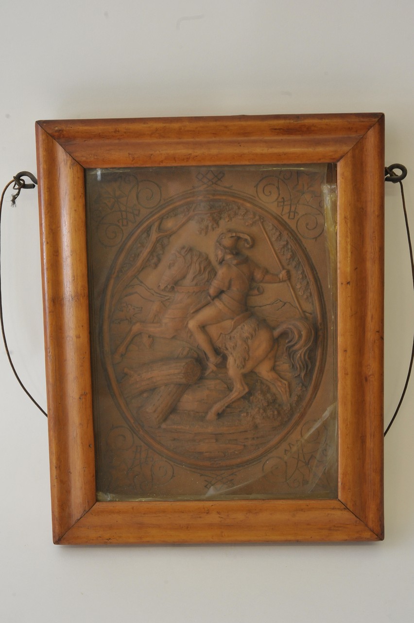 A maple framed carved wooden plaque, well detailed in raised relief depicting a figure on horseback