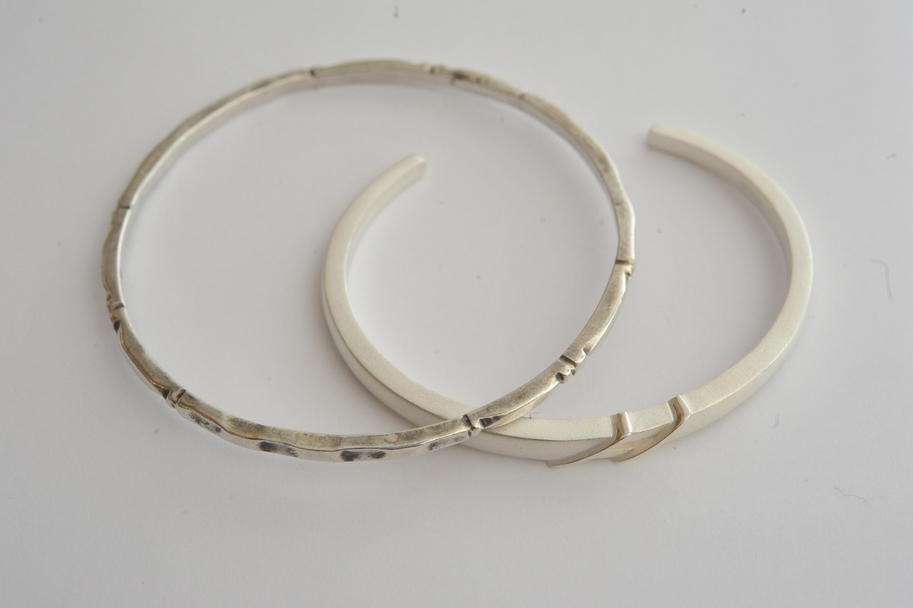 Two silver bangles, one open torque with matte finish, the other full ring