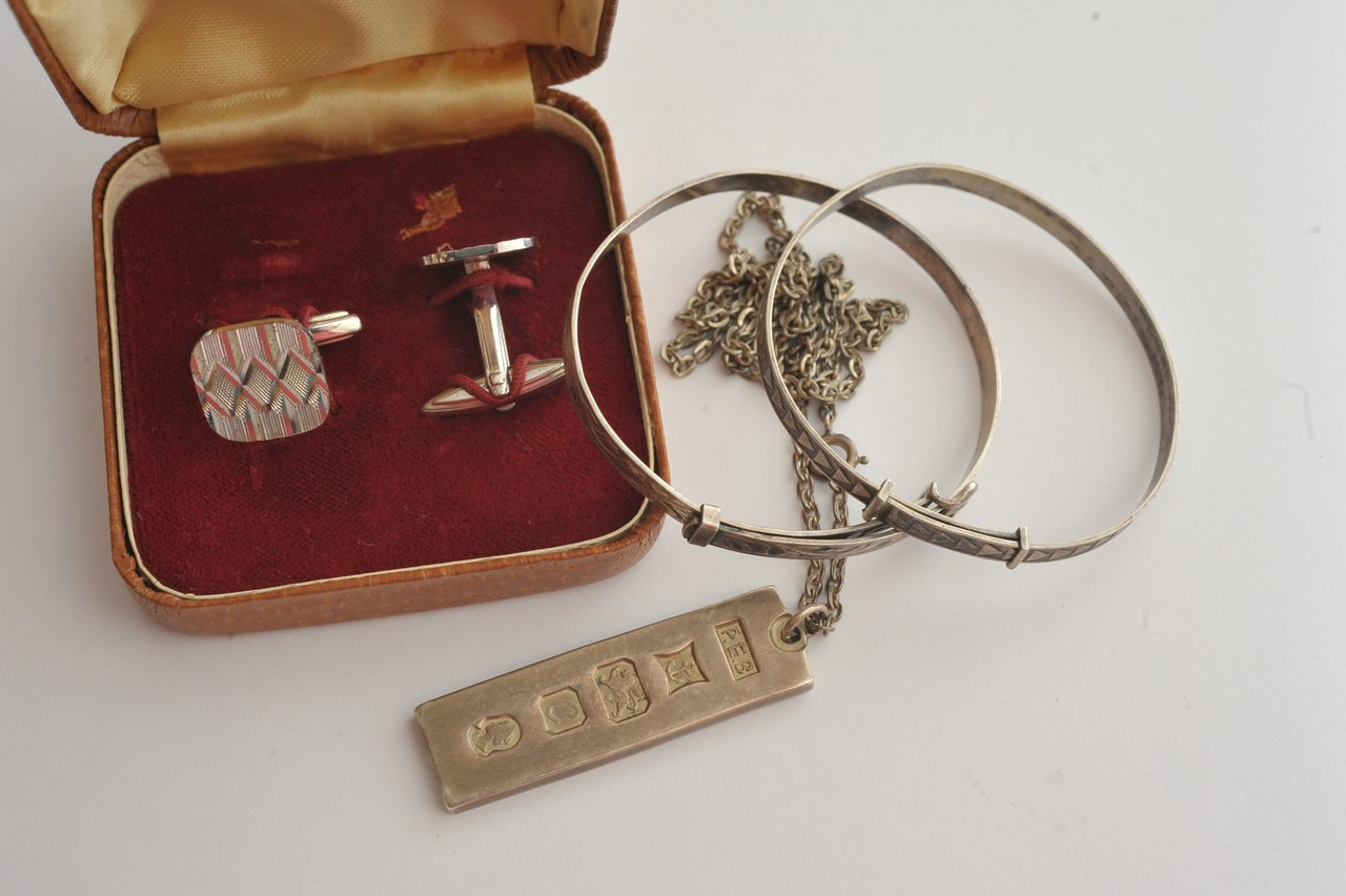 A small bag of silver jewellery comprising two bangles, cuff links and ingot pendant