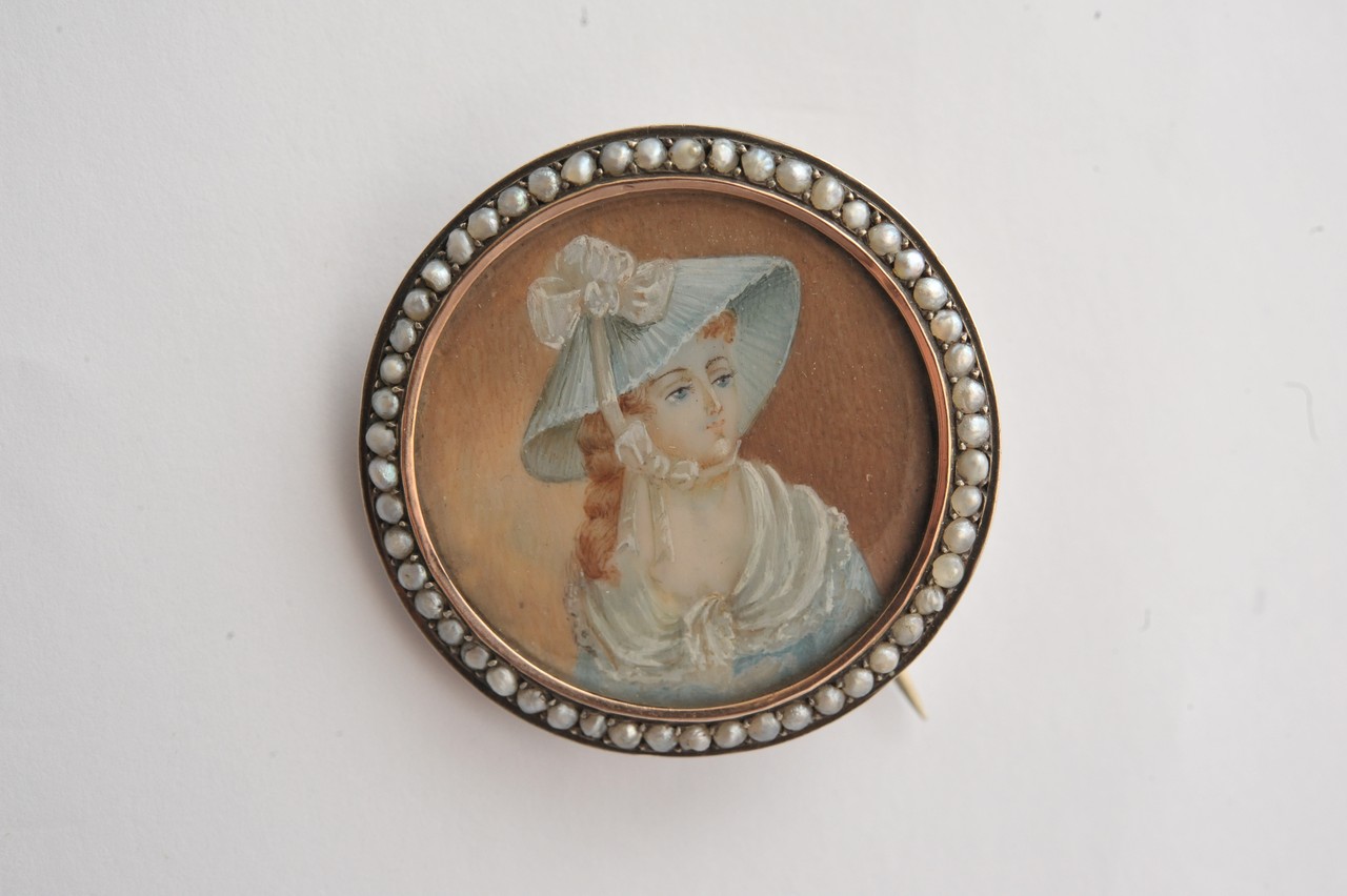 A white metal brooch of circular form inset with a portrait miniature on ivory with seed pearl