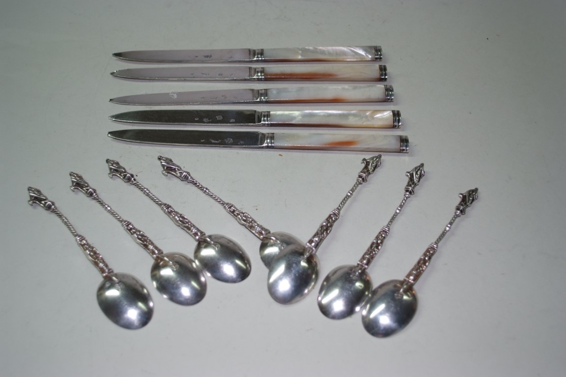 A set of seven Hanau silver teaspoons, decorated figures to terminals; together with a set of five